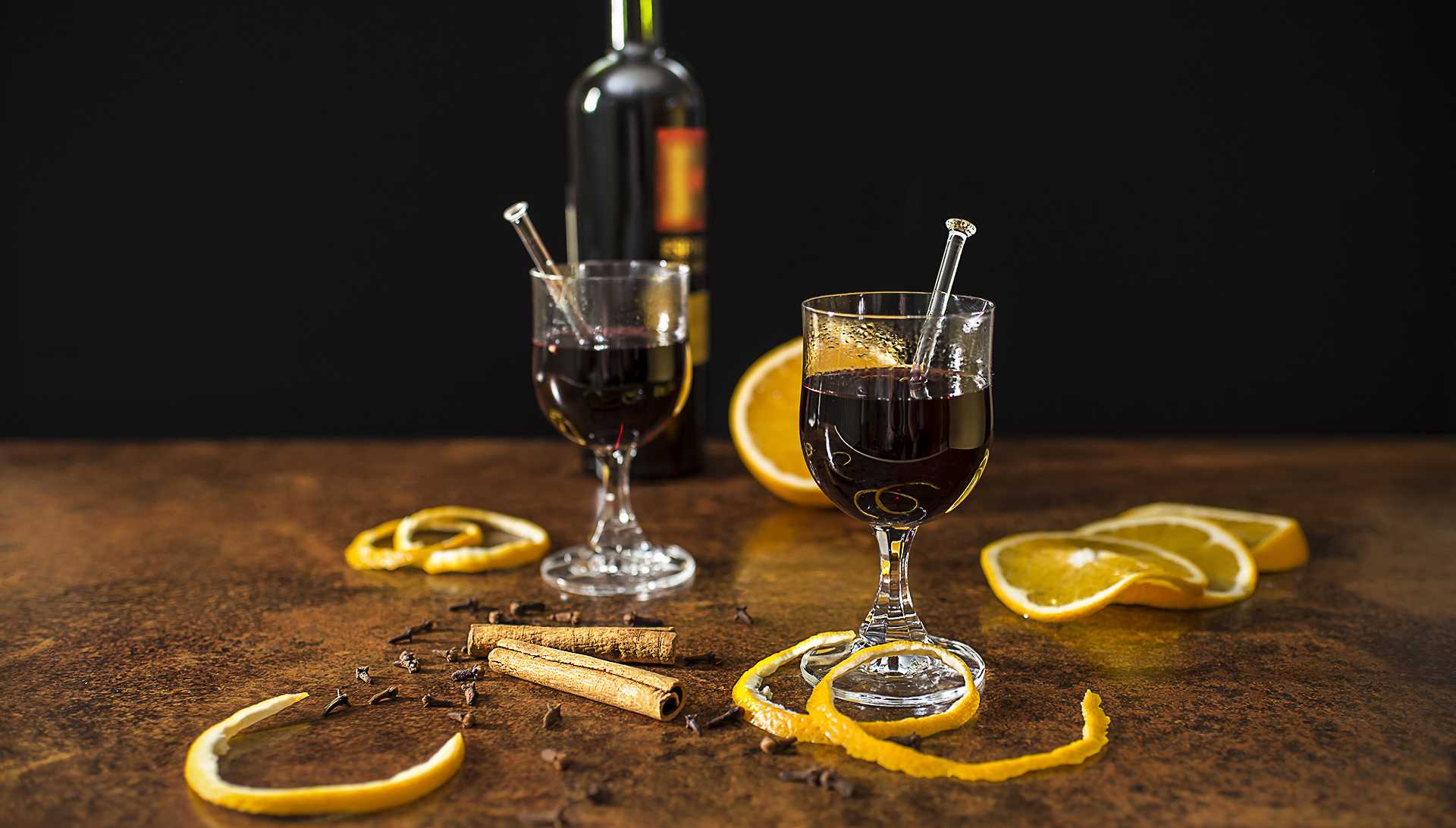 Mulled wine with spices and oranges close up in front of black background